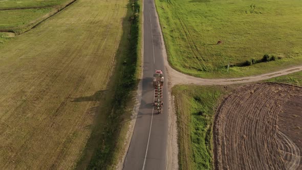 Farmer on a Tractor with a Plow in a Transport Position Rides on a Narrow Asphalt Road in the alt