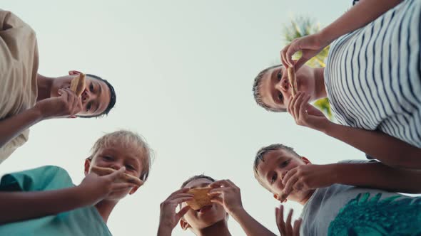 Low Angle Shot Group of Children Friends Picnic Eat Pizza Sit on Park Grass Chewing and