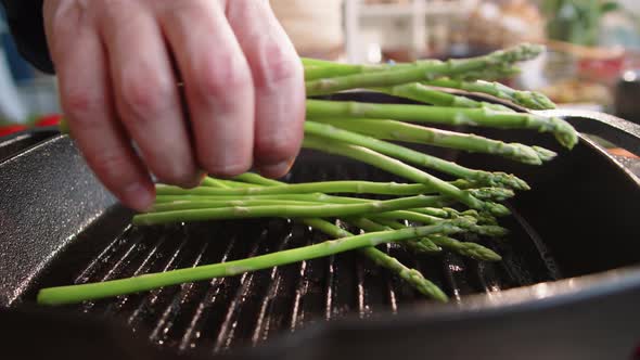 Chef Putting Fresh Asparagus on Grill Pan alt