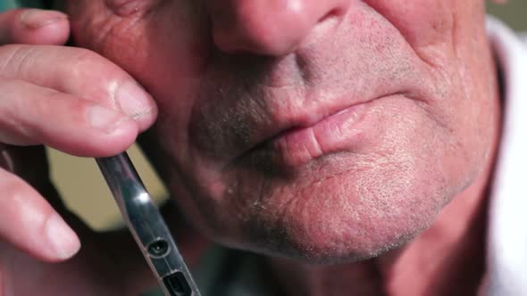 Close-up face of a Caucasian elderly man talking on the phone on a serious topic. Parts of the face alt