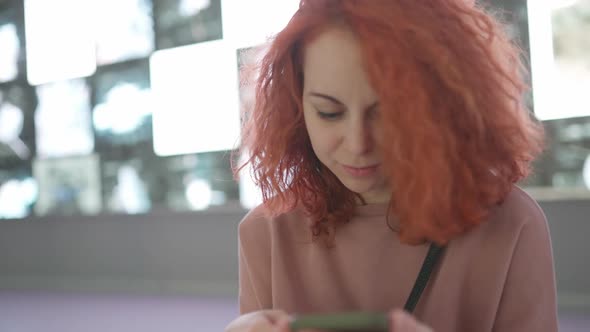 A girl with red hair looks at her smartphone while doing something alt