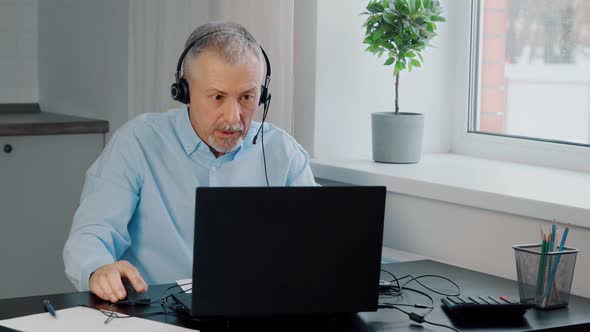 A Focused Businessman Wearing Headphones Takes Part in Online Negotiations