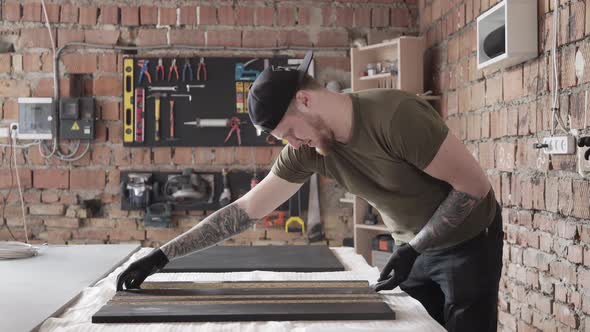 Skill Bearded Craftman Working Standing at the Table in Garage. A Man Works in a Workshop. The Board alt