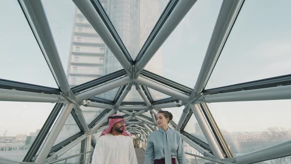 Diverse Business Couple Walking Along Glass Bridge alt