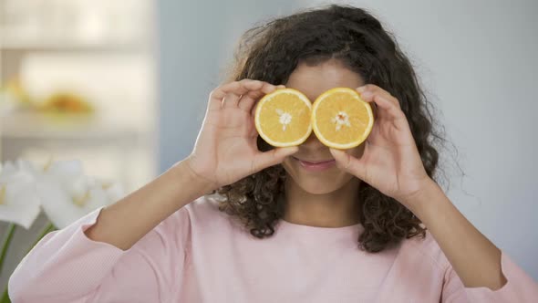 Mixed Race Girl Smiling at Camera, Holding Halves of Oranges Before Eyes, Health alt