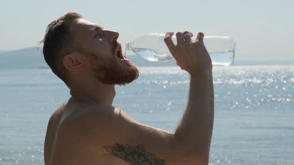 Sexy Young Man with Red Beard with Tattoo on His Shoulder Beautifully Drinks Water From Bottle alt