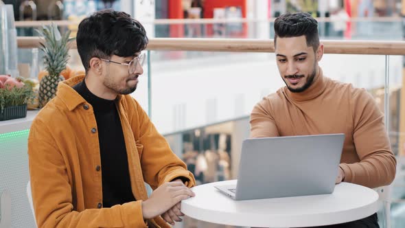 Happy Young Guys Friends Sitting in Cafe Arab Man Showing on Laptop Achievement New Project Great alt