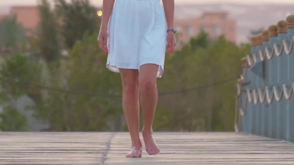 Closeup of Young Woman in White Dress Walking on Long Pier in the Evening alt
