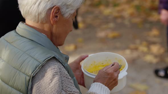 Gray Haired Old Woman Eating Charity Meal While Sitting on the Bench in the Park alt
