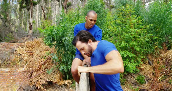 Male trainer assisting fit man to climb over wooden wall during obstacle course 4k alt