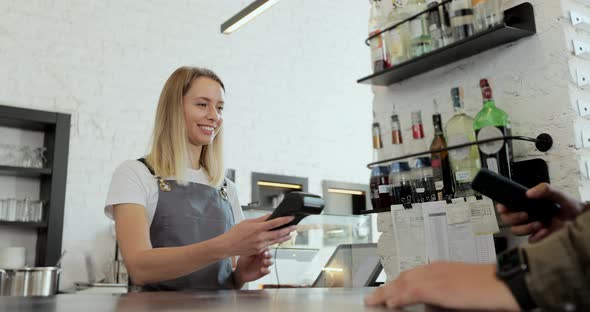 In the Cafe Woman Makes Takeaway Coffee for a Customer Who Pays By Contactless Mobile Phone to alt
