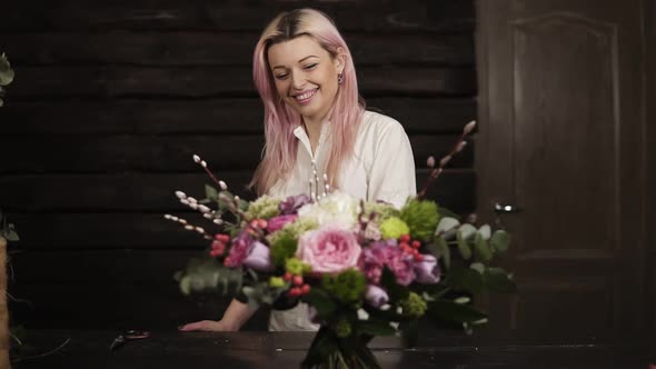 A Beautiful Girl with Pink Hair Smiles Admires a Stunning Bouquet of Flowers Lying on the Surface alt