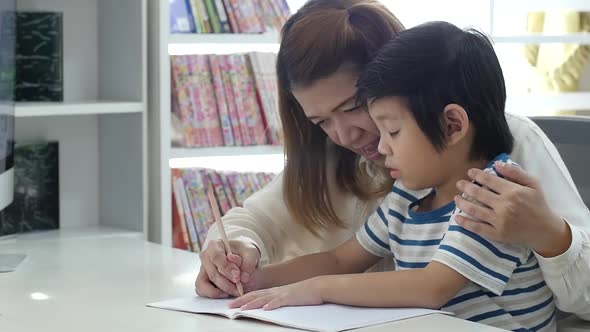 Asian Mother Helping Her Son Doing Homework On White Table Slow Motion alt