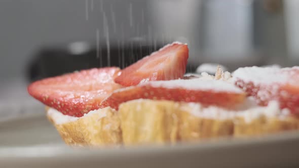 Extreme Close Up Powdered Sugar is Poured Onto Croissants with Strawberry alt
