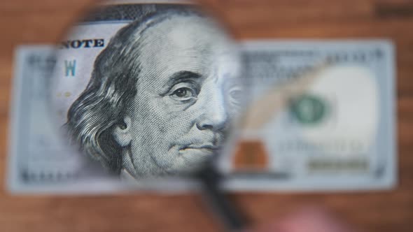 One Hundred Dollars Look Under Magnifying Glass on Wooden Table alt