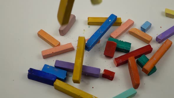 Sticks of multicolored chalks fall on a white background, slow motion