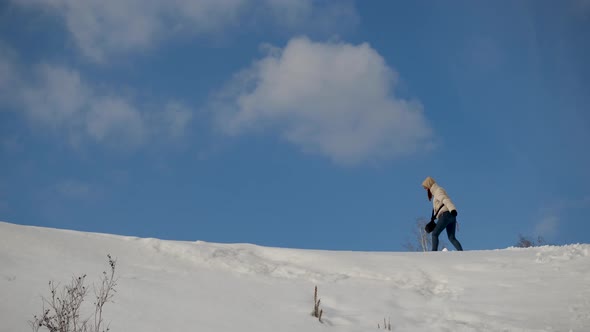 A Girl Traveler in a Jacket Climbs Up a Snowy Mountain Against the Cloudy Sky