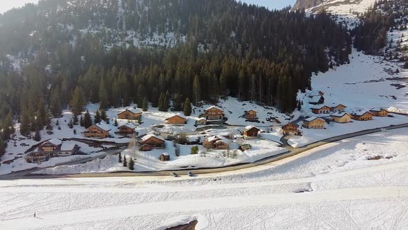 Drone shot ing backwards) of Chalets in the French Alpine Mountains with a Forest in the Background alt