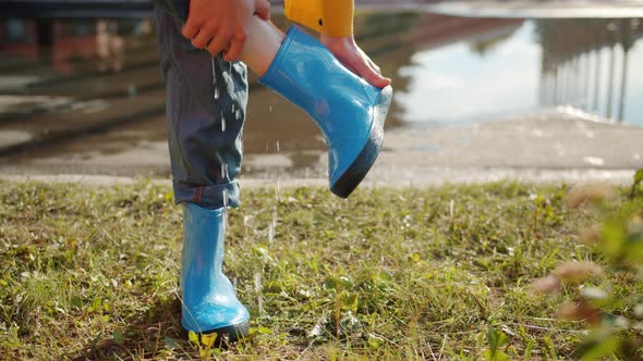 Close-up of Hand Taking Off Rubber Boot From Bare Foot and Pouring Out Water alt