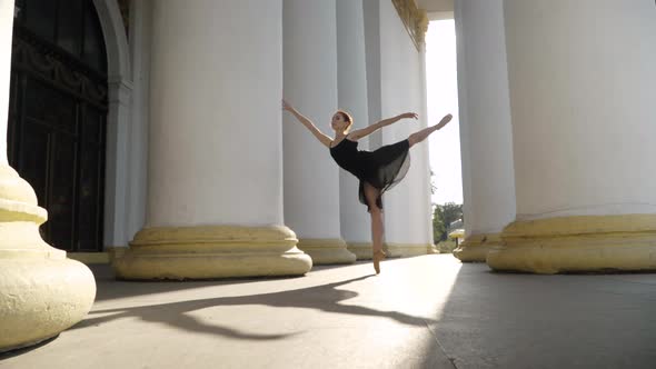 Wide Shot of Slim Young Ballerina Standing on Tiptoes on One Leg in Sunlight alt