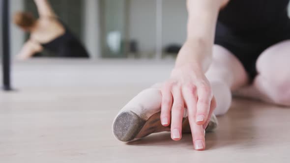 Caucasian female ballet dancer stretching up on the floor for dance class in a bright studio alt