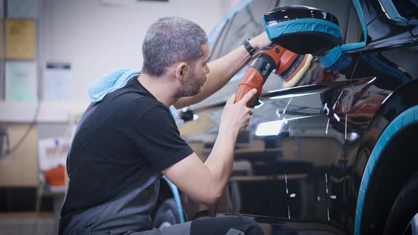 An Experienced Detailing Studio Worker Polishing a Car alt