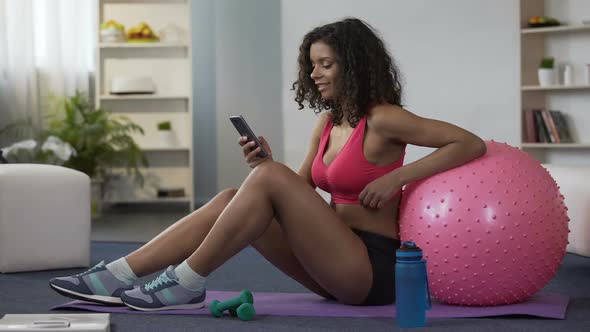 Biracial Woman in Gym Outfit Sitting on Floor, Using Mobile Phone, Application alt