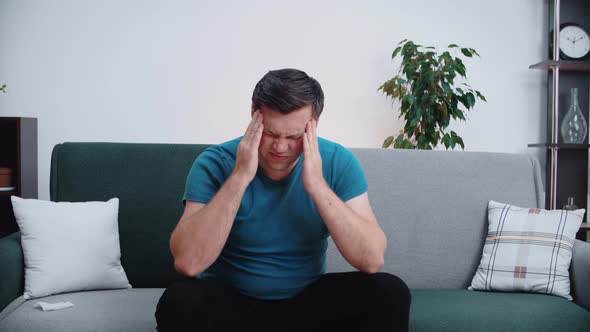Man suffering from severe headache or migraine, sitting on sofa