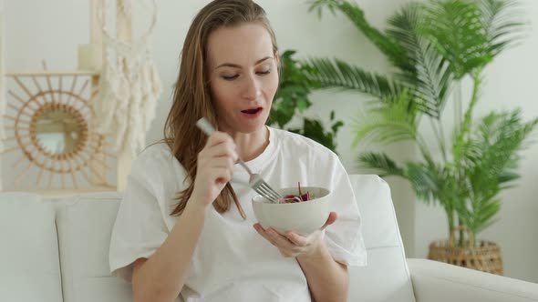 Happy Brunette is Relaxing on the Couch and Eating a Vegetable Salad at Home alt