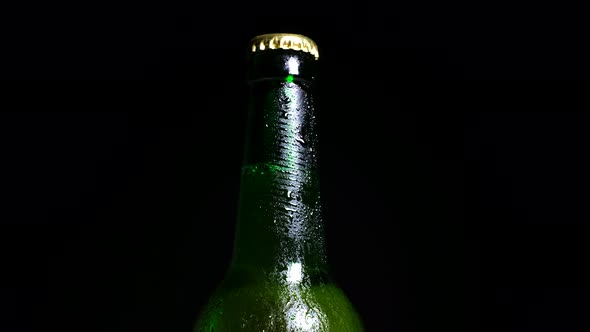 Cold Beer with Water Drops on Bottle is Illuminated By Light From the Darkness