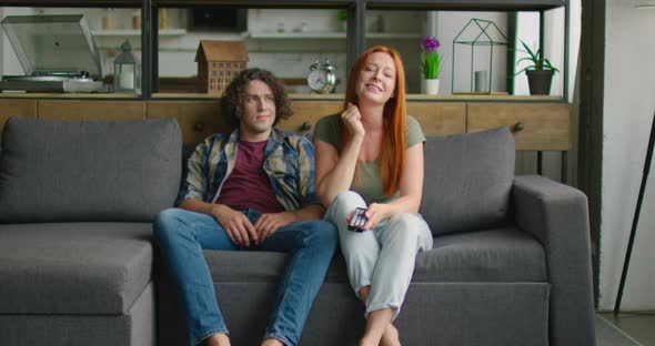 Young Couple Is Sitting on Sofa, Woman Is Watching TV, Man Is Bored alt