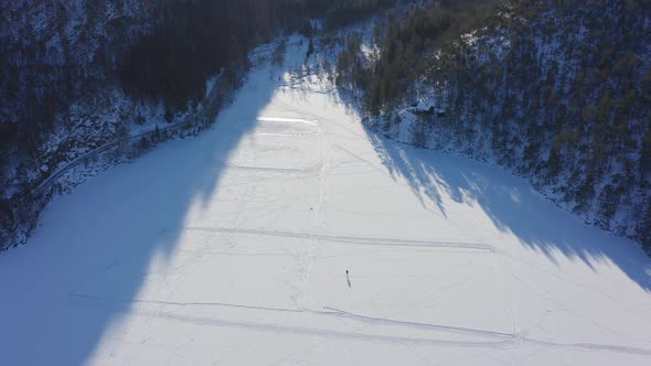 Aerial top down view single person ice skating on frozen lake - Wide Snowy Landscape alt