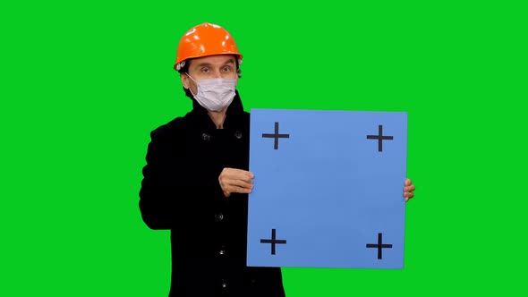 Builder In Hardhat And Mask Something Presenting And Holding Blue Billboard