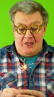 Caucasian Mature Adult Man Blows Hard on Sparkler and Wonders That He Cannot Extinguish It alt