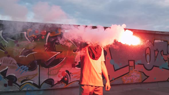 Young Man in Balaclava with Red Burning Signal Flare on the Roof with Graffiti Background Slow alt