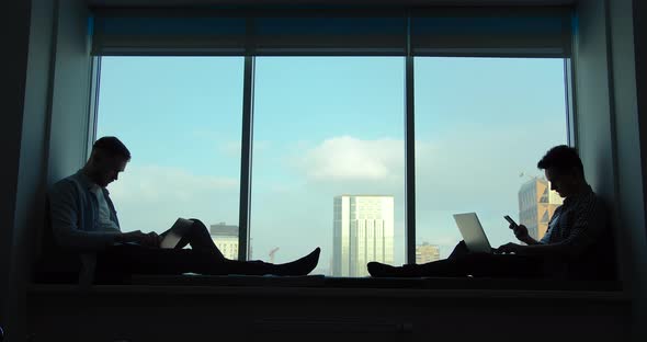Businessmens Sit on the Windowsill in the Office Facing Each Other alt