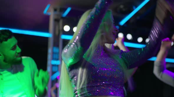 Slim Confident Party Girl Dancing in Night Club with Blurred People at Background alt