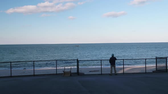 Man Overlooking Beach on Boardwalk With Fence Aerial 2
