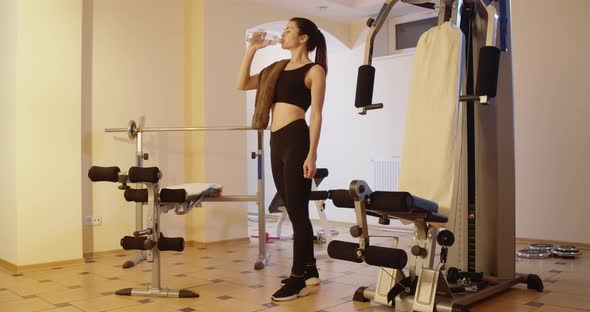 Wide Shot Portrait of Slim Beautiful Sportswoman Drinking Refreshing Water Standing in Gym and alt