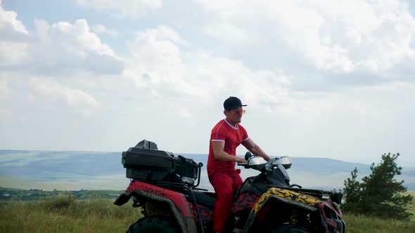 Man in a Black Cap and Red T-shirt on a Colored ATV Rides alt
