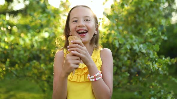 Cute girl with braces eating italian ice cream cone smiling while resting in park on summer day,