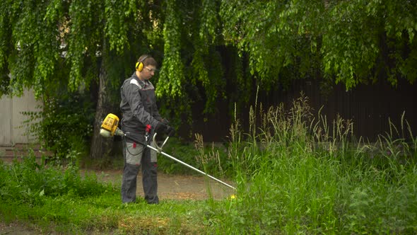 A Young Man From the Special Services Mows the Lawn with a Petrol Trimmer alt