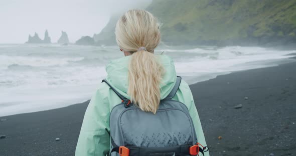 Woman with a Green Raincoat Walking on a Black Sand Beach Enjoying View to Reynisfjara Sea Stack