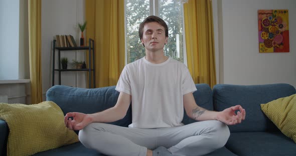 Front View of Young Man Meditating Alone at Home Natural Light Slow Motion. Attractive Person with