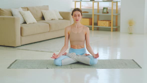 Relaxed young woman in sportswear is meditating in lotus position sitting on yoga mat alt