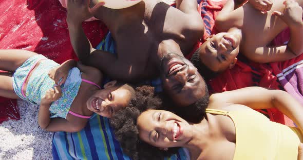 Portrait of smiling african american family lying on towels on sunny beach alt