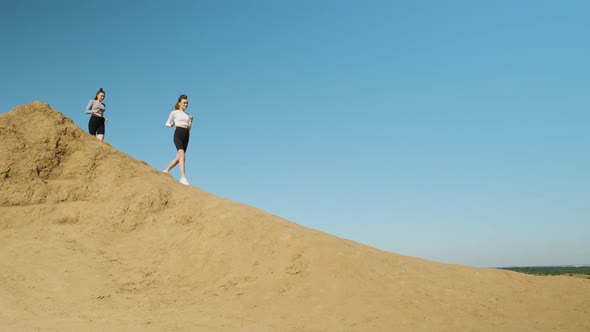 Two Slender Athletic Women in Sportswear and Black Shorts are Doing Marathon Run Running Down Sandy alt