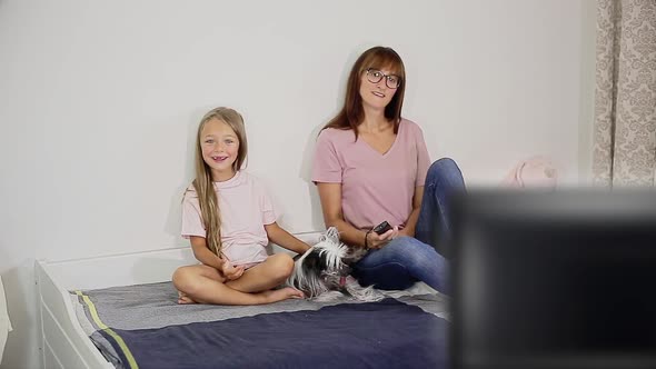 A Woman with a Child and a Dog Sitting on the Bed Watching Tv