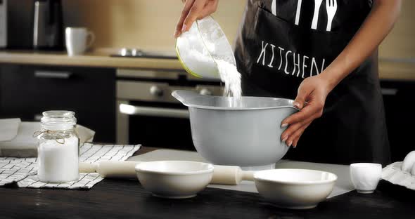 Woman Pouring Flour Into a Gray Bowl and Kneading Dough with Her Hands