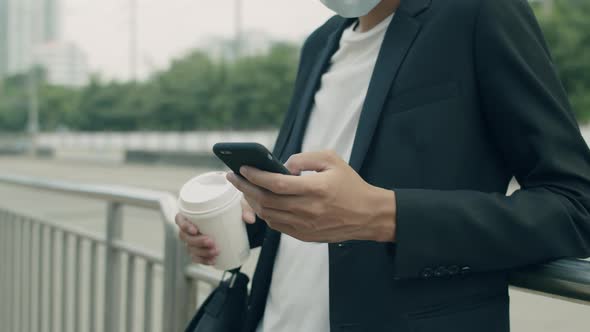 Asian businessman standing beside fence using his smartphone while walking on the street.